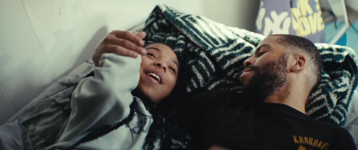 Father and daughter lie in bed in a sunlit room playfully touching and tickling each others faces