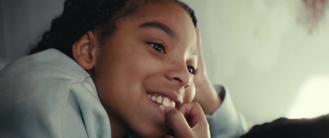 Closeup of a girls face as she sits comfortably on a couch being caressed by an adult