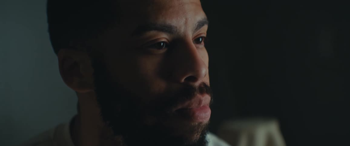 A close up of the face of a bearded man sitting on a dimly lit room