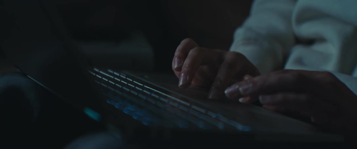 A closeup of hands using the touchpad of a laptop in a dimly lit environment