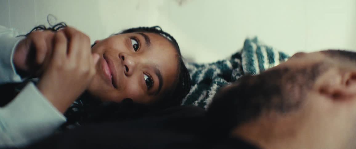 Father and daughter lie in bed in a sunlit room playfully touching and tickling each others faces