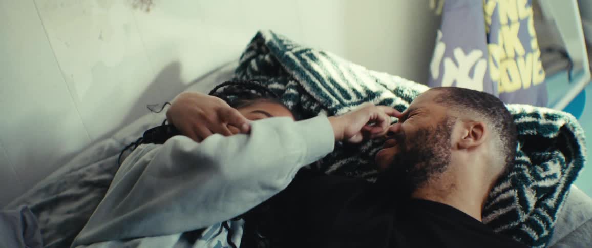 Father and daughter lie in bed in a sunlit room playfully touching and tickling each others faces