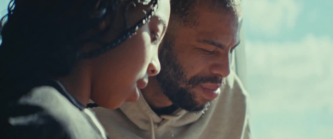 A father helps his daughter with a task in a sunlit room