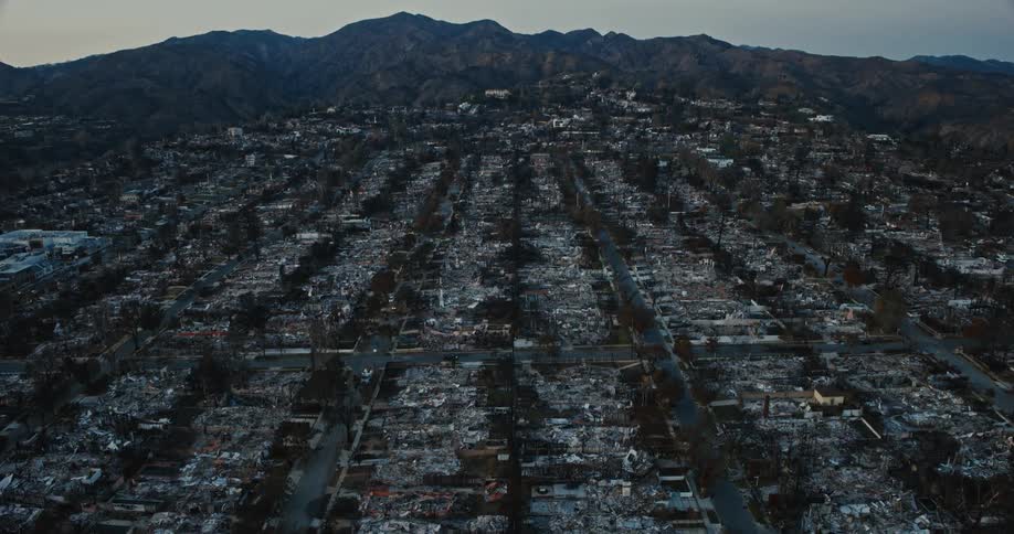 Aerial view pans down to show the charred remains of a suburb with destroyed homes roads and cars amidst rolling hills
