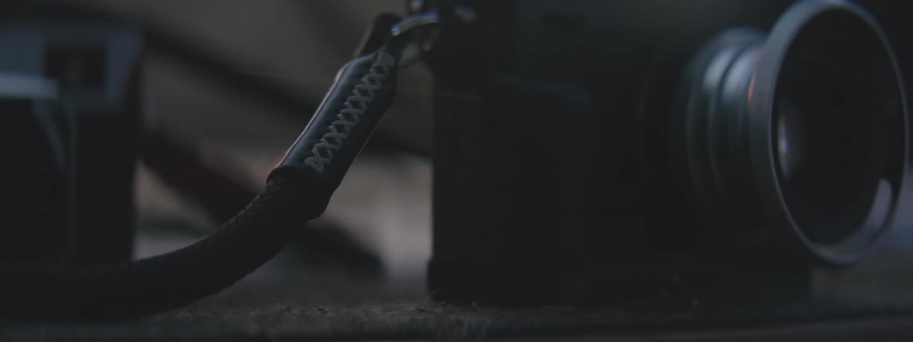 Closeup of a hand placing the braided strap and lens of a vintage camera in a lowlight environment