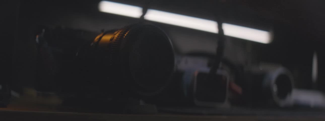 A person carefully arranging vintage film cameras over a table in a dimly lit room illuminated by a soft fluorescent light