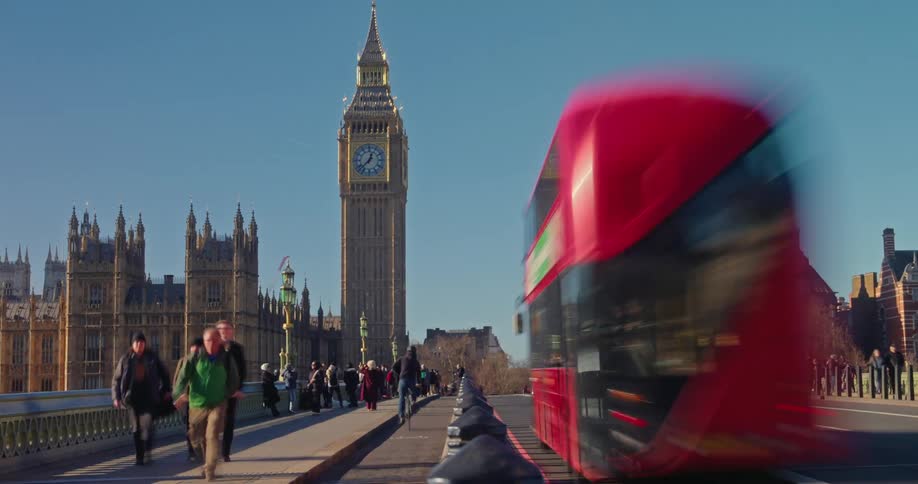 Vehicles and people travel past a tall clock tower