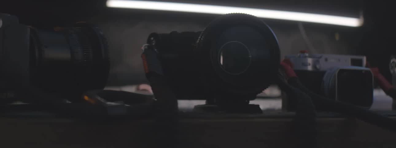 Cameras and photographic equipment are arranged on a table in a dimly lit environment