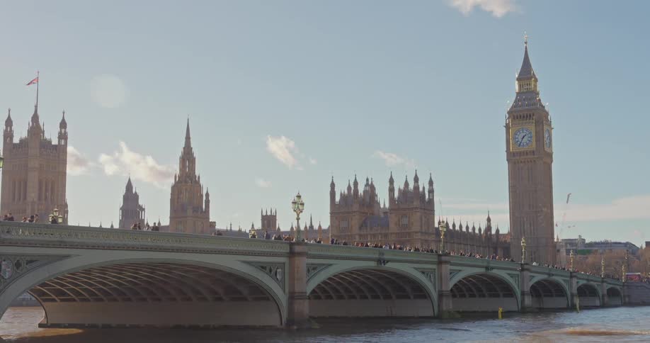 A daytime shot features westminster bridge spanning a river with the palace of westminster and big ben visible in the background against a partly cloudy sky