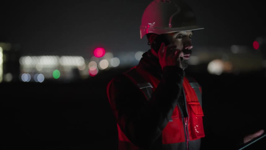 Man in helmet in vest is outdoors at night talking on cell phone