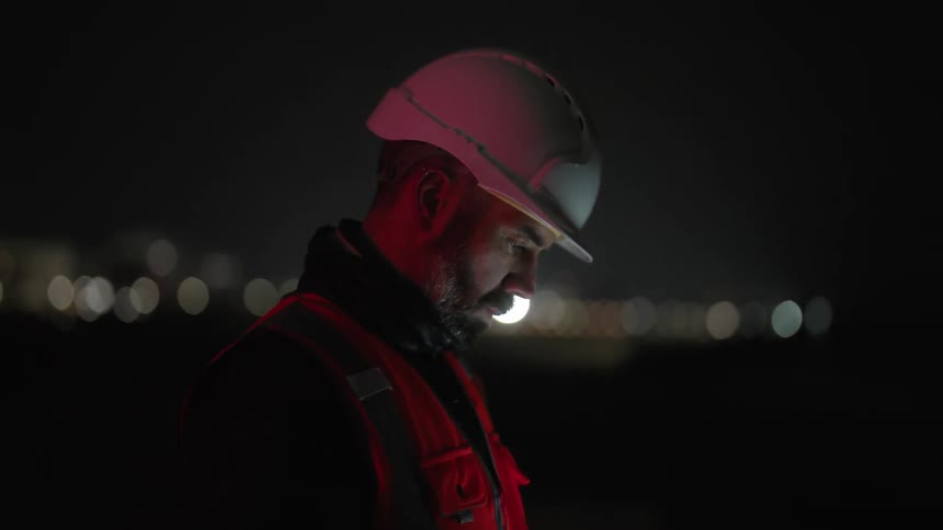 Man in white helmet and protective vest stands outdoors at night