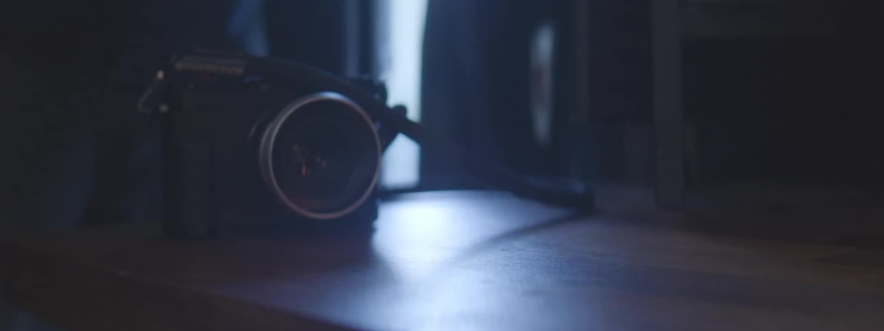 A person alternates between picking up vintage film cameras to take pictures out of a window in a dimly lit room