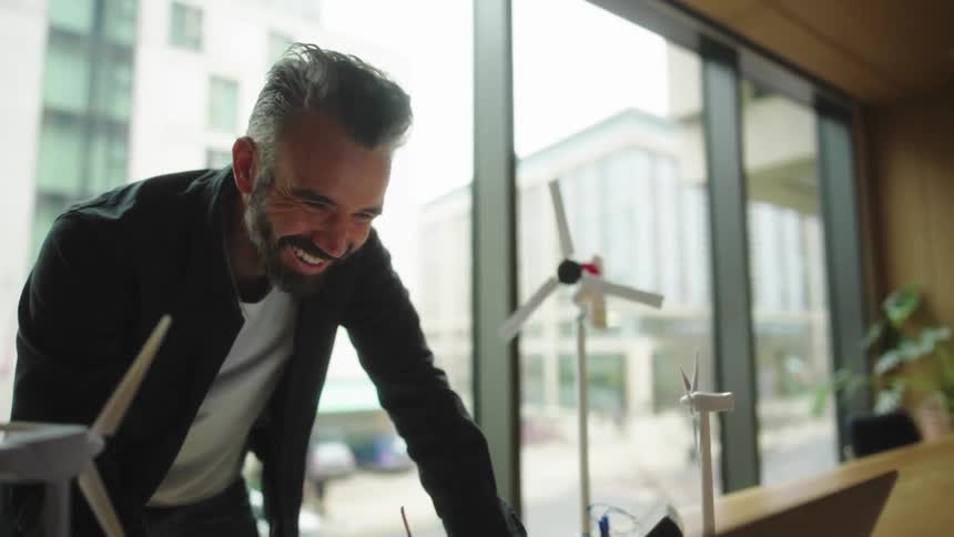 Smiling man in a bright office while working with wind turbine models on the table