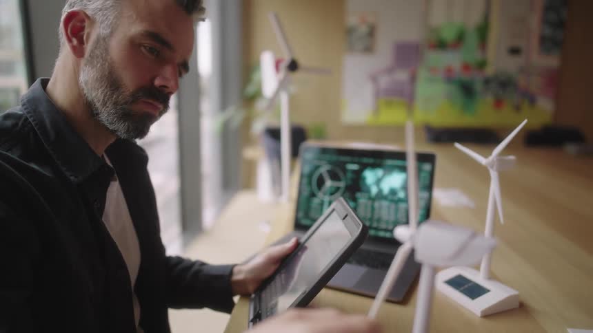 Man sitting at a table next to an open laptop and interacting with an abstract prototype of a wind energy platform