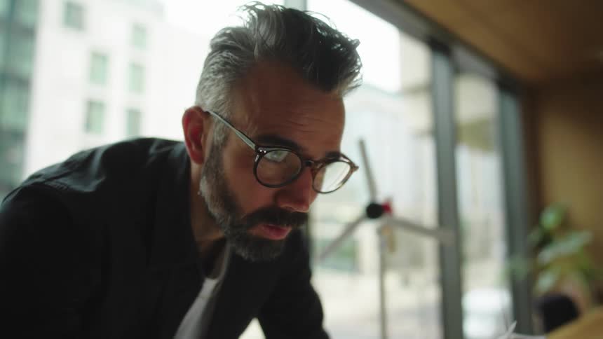 A man standing in a room looking at a laptop and then puts glasses on his face