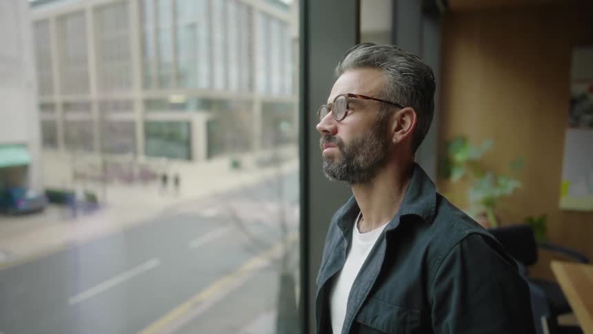 A man is looking at the city from an office window