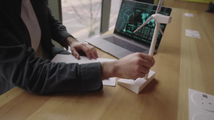 A man works tirelessly at his desk on his laptop and looks at a mini turbine