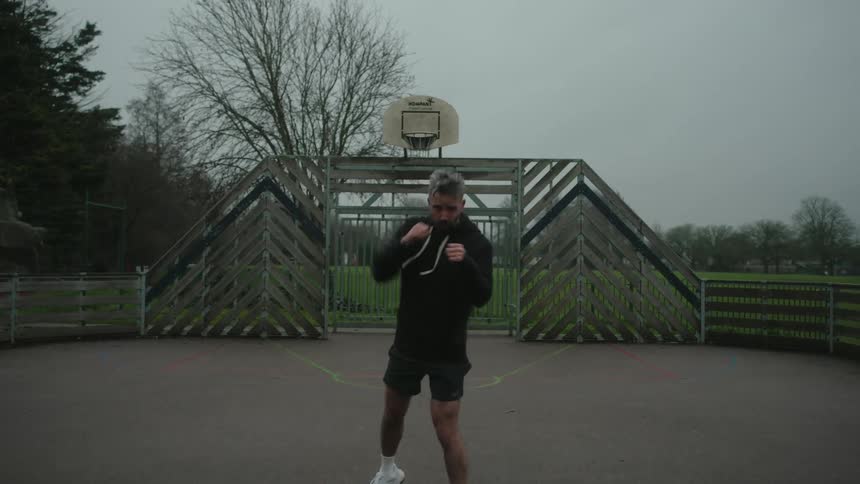 Man practices boxing on an outdoor court under a cloudy sky