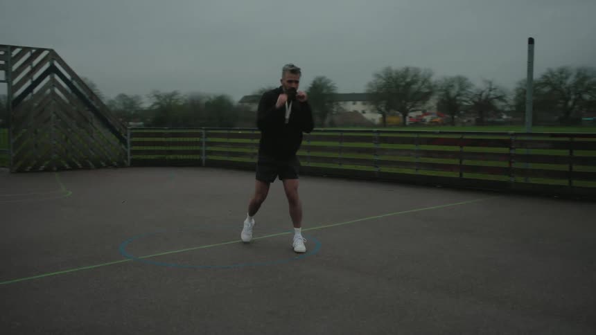Man outdoors next to a field practicing boxing punches