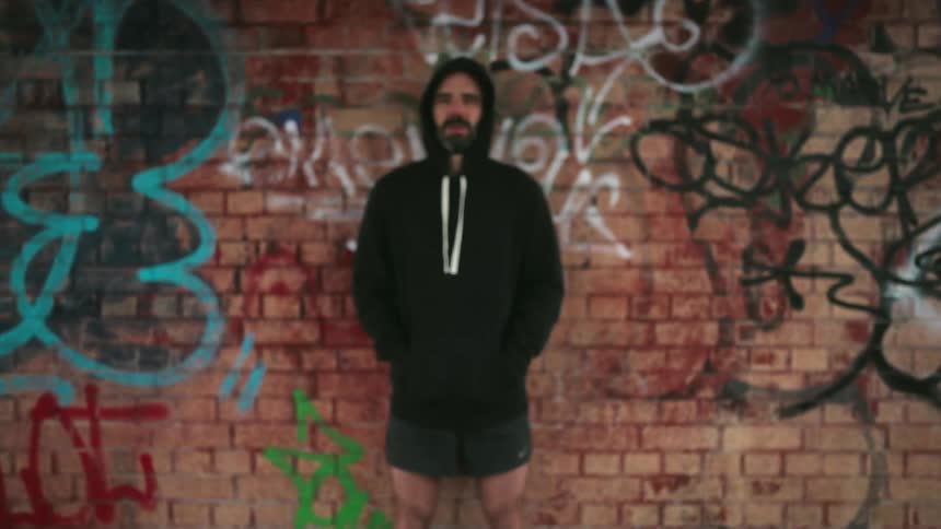 Man is smiling as he stands in front of a brick wall covered in graffiti