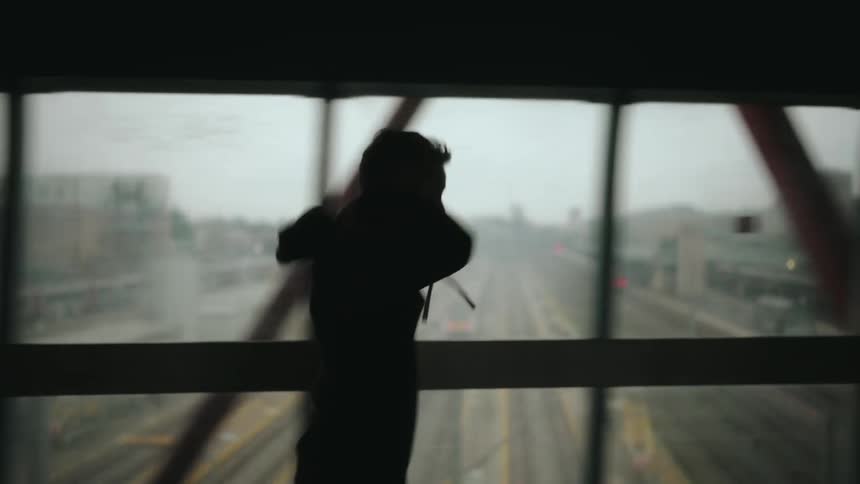 The silhouette of a person in a hoodie jogging on an overpass above a highway