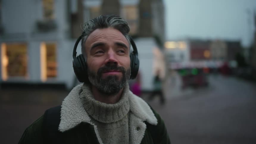 Man with headphones and backpack looks at something above with a smile