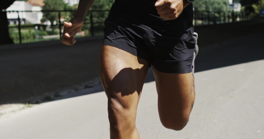 Closeup of the legs of a runner in black shorts moving in the sunlight