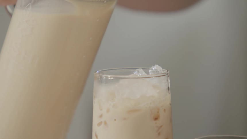 A creamy drink is being poured over a glass full of ice
