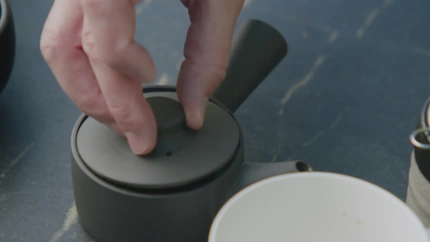 A mans hand places a cover on a tiny pot with spices and clear liquid in it