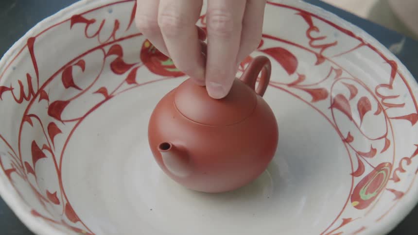 Hand closing a small teapot with hot tea