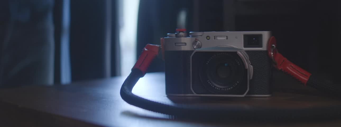 Vintage camera with red strap rests on a table in a dimly lit room