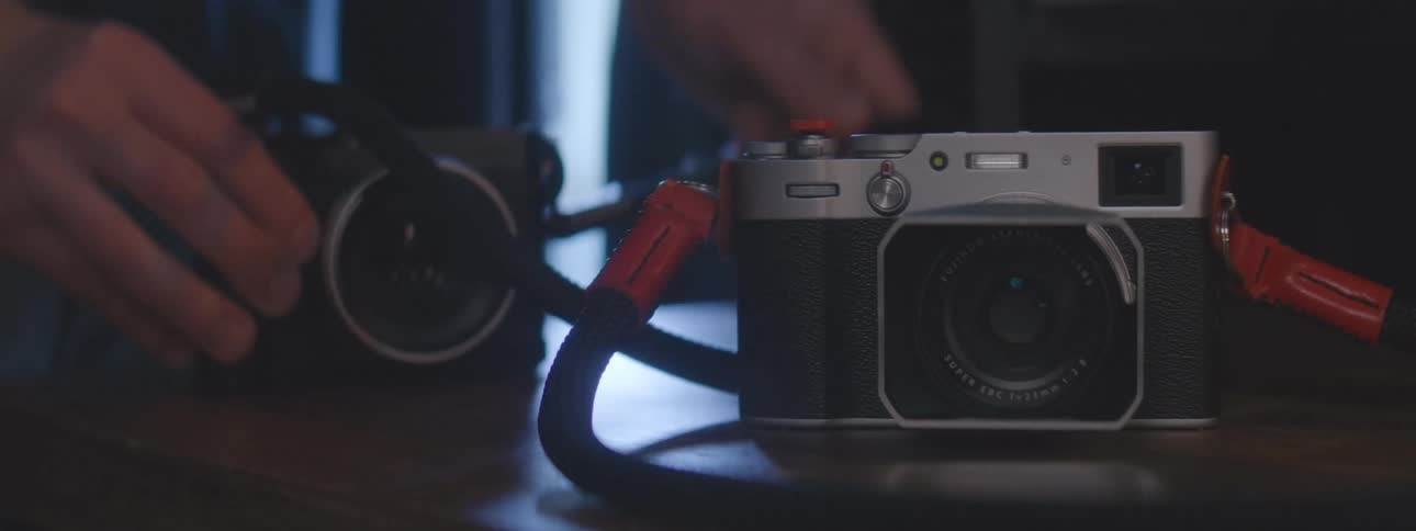 Two cameras are on a table a person picks up one and puts it down then does the same with the other