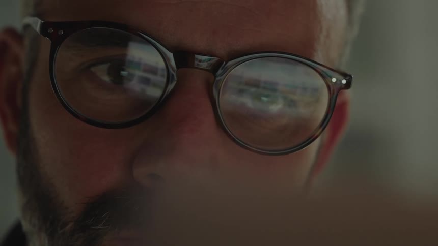 Computer screen reflected in the glasses of a concentrated man