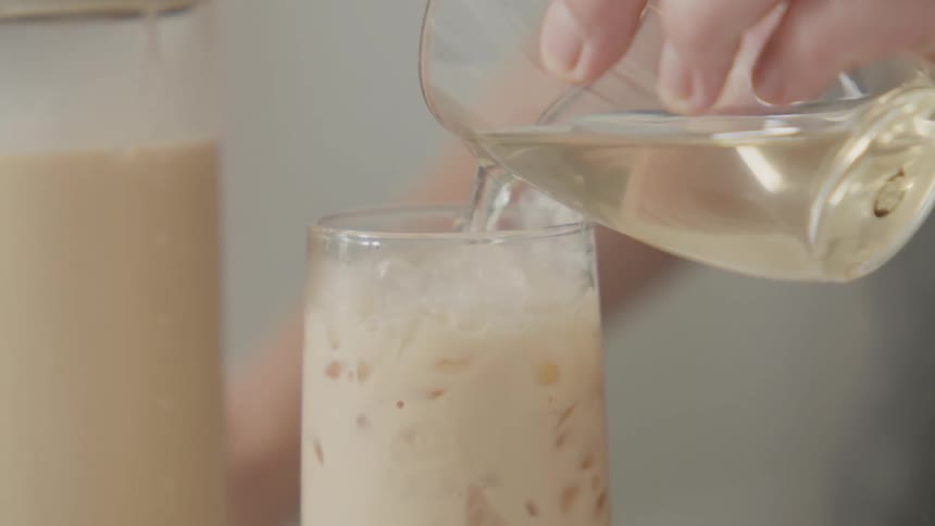 Hand holding a glass with liquid and pouring it into another glass with milk and ice