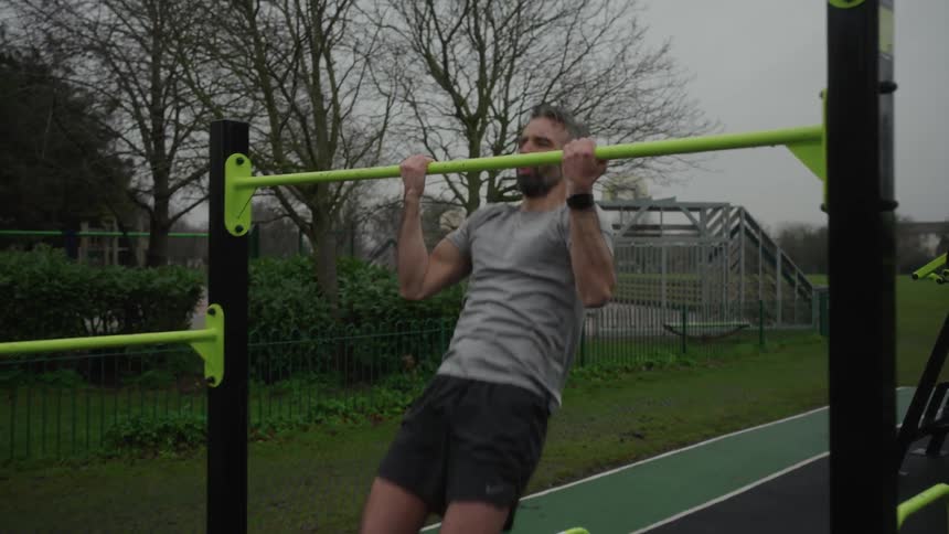 Man does pullups in an outdoor park under a cloudy sky