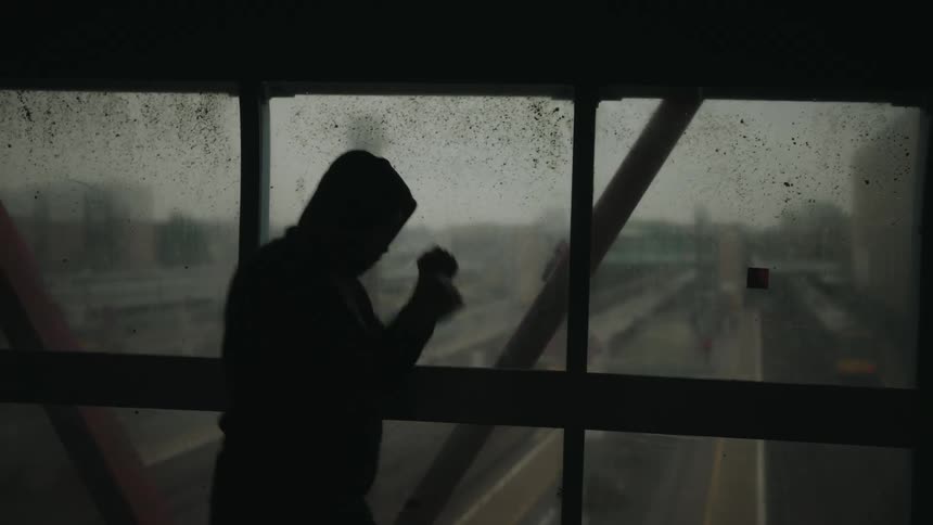 The silhouette of a person in a hoodie boxing on an overpass above a highway