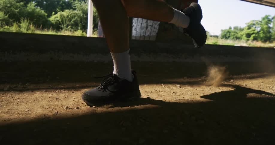 Closeup of a man jogging on dusty soil under a bridge