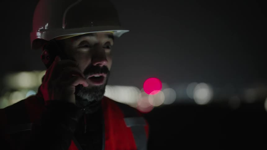 A construction worker is talking on his phone outdoors at night