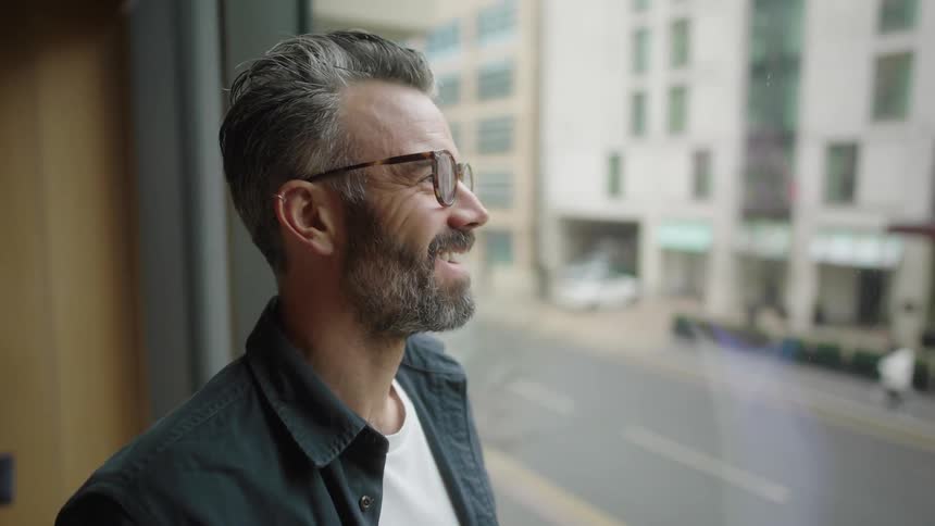 A man is happy and smiling as he looks out the window