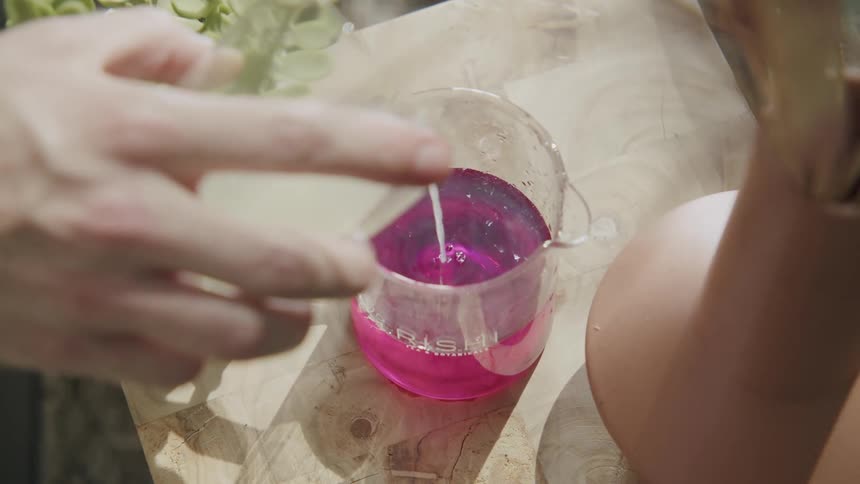 Clear substance is poured into a beaker containing pink liquid