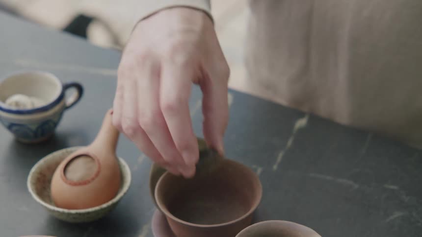 A persons hand places a disc of puerh tea into a ceramic bowl on a table