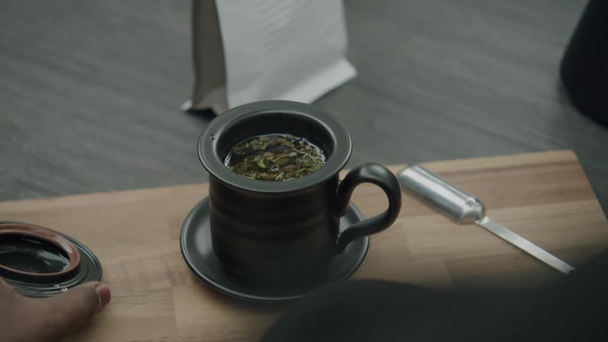 Person opens the lid of a black cup with herbal tea on a wooden board