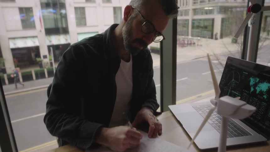 Man writes something down on a piece of paper while working on a renewable energy project with miniature wind turbines