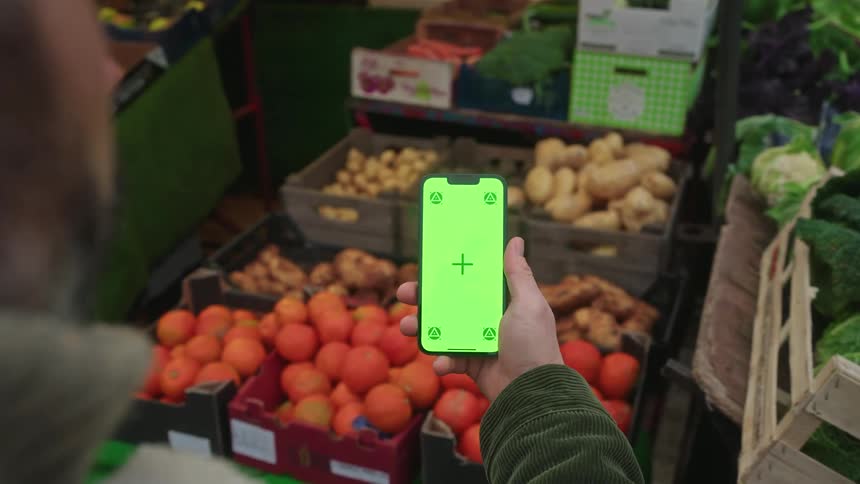 Person holds a smartphone at an openair vegetable and fruit market