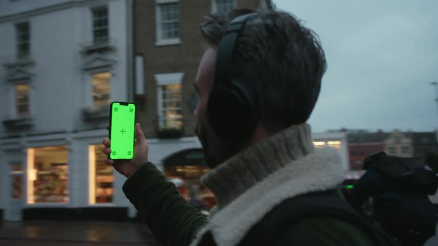 Man with headphones and backpack holds a smartphone