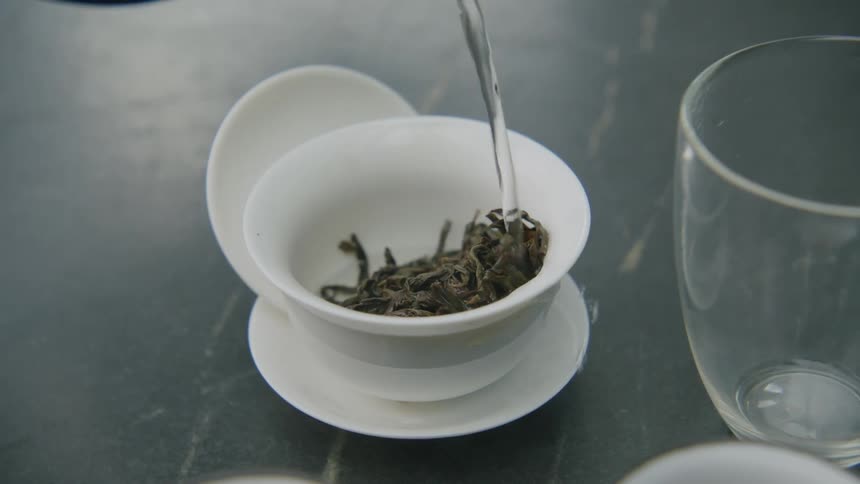 Liquid being poured into a white ceramic mug containing herbs
