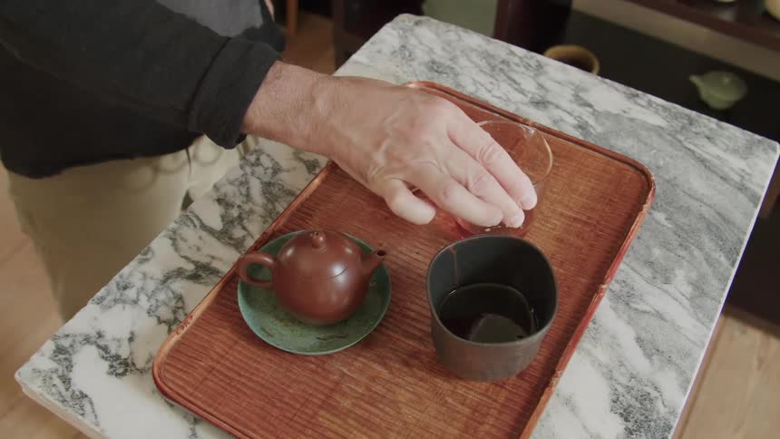 A persons hand serving puerh tea into a ceramic bowl on a tray