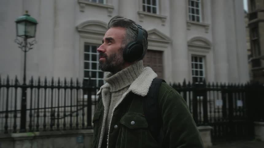 Man with headphones looks around as he walks in front of a historic building