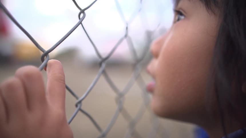 A child looks through a chainlink fence