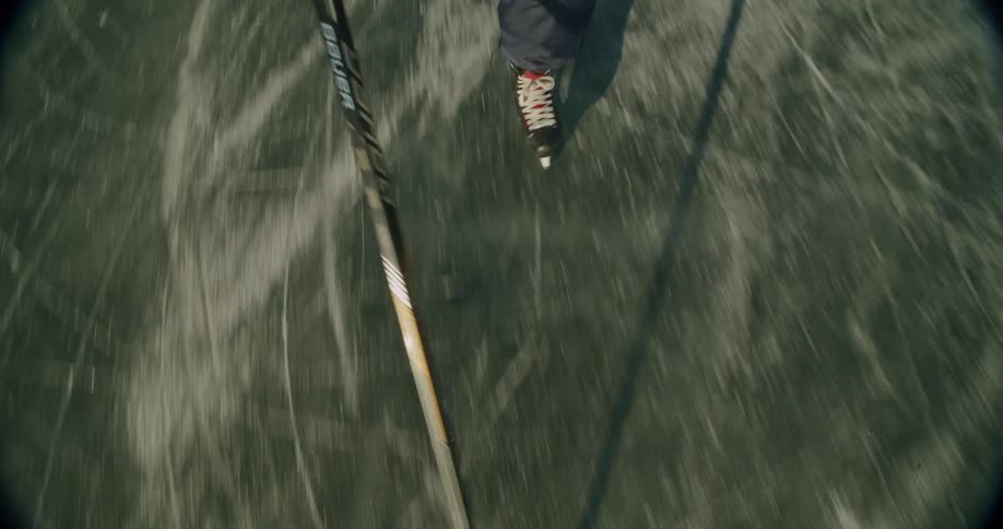 A hockey player wearing skates and holding a hockey stick glides across an ice rink